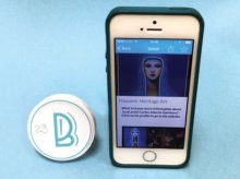 A BluuBeam beacon sits next to a smartphone that’s displaying a